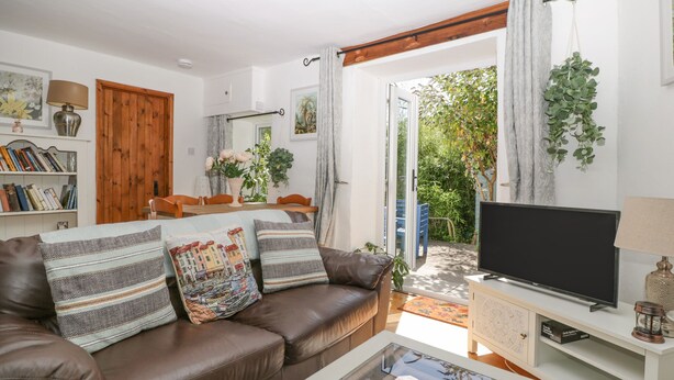 A cozy living room with a brown leather sofa, a glass coffee table, a flat-screen TV on a white cabinet, and a bookshelf filled with books. - Mackerel Cottage (Budleigh Salterton)