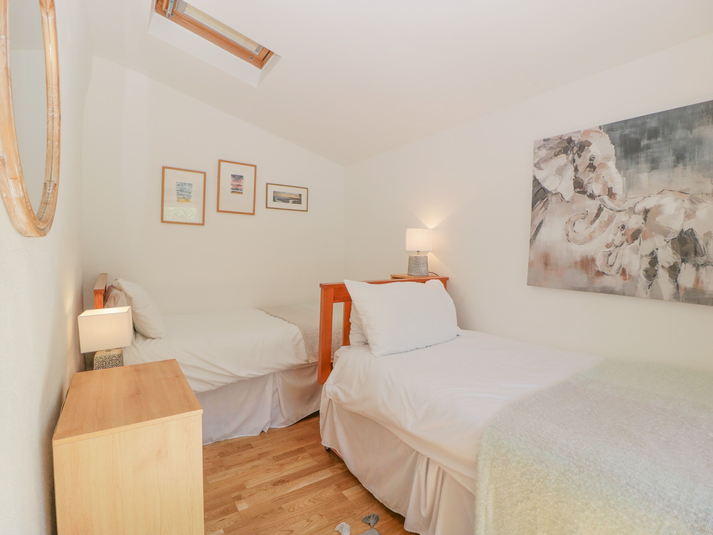A bedroom with two beds, wooden flooring, a desk, and a painting on the wall.