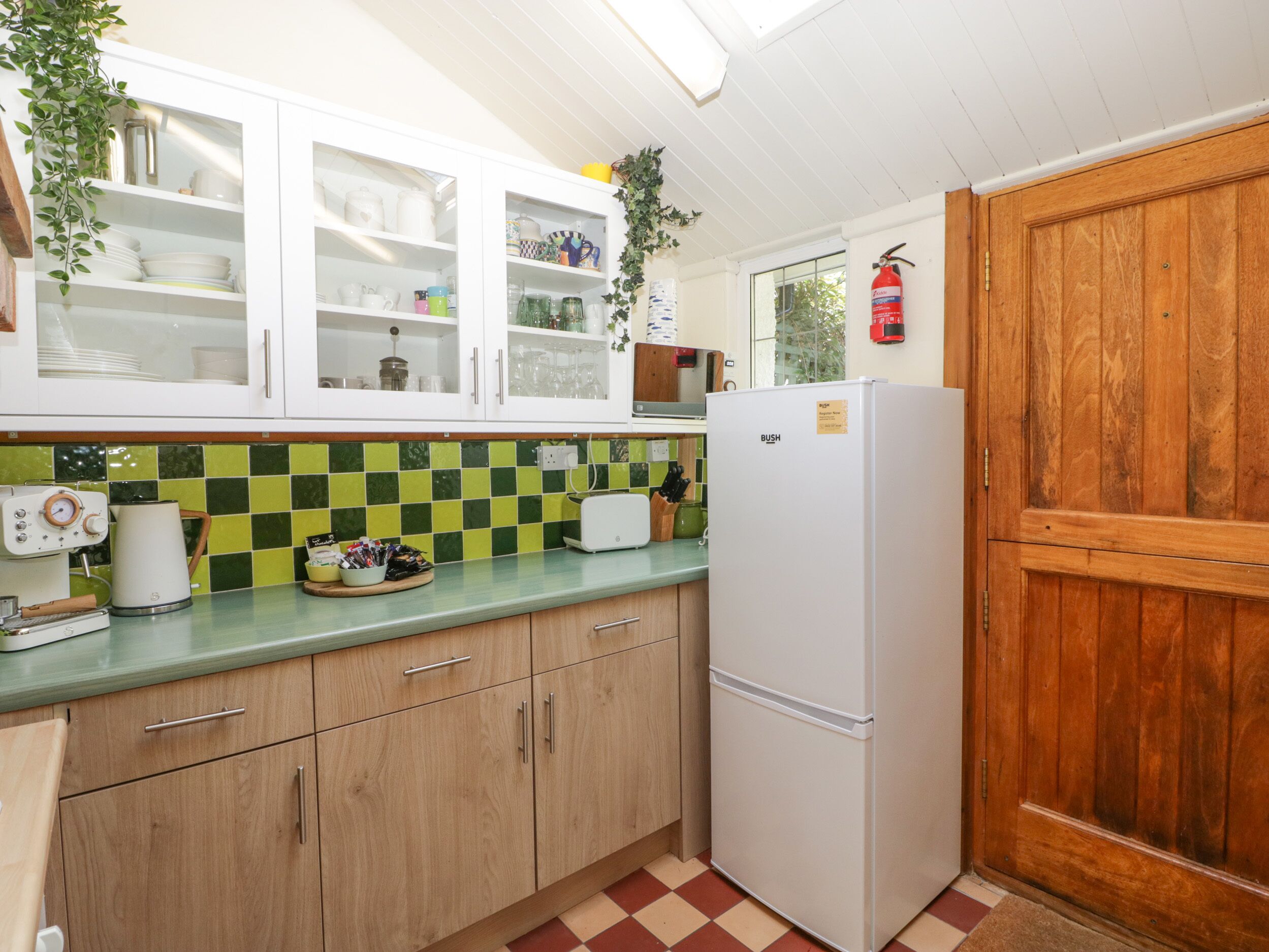 A kitchen with white cabinets, a green and white checkered backsplash, a white refrigerator, and a wooden door.