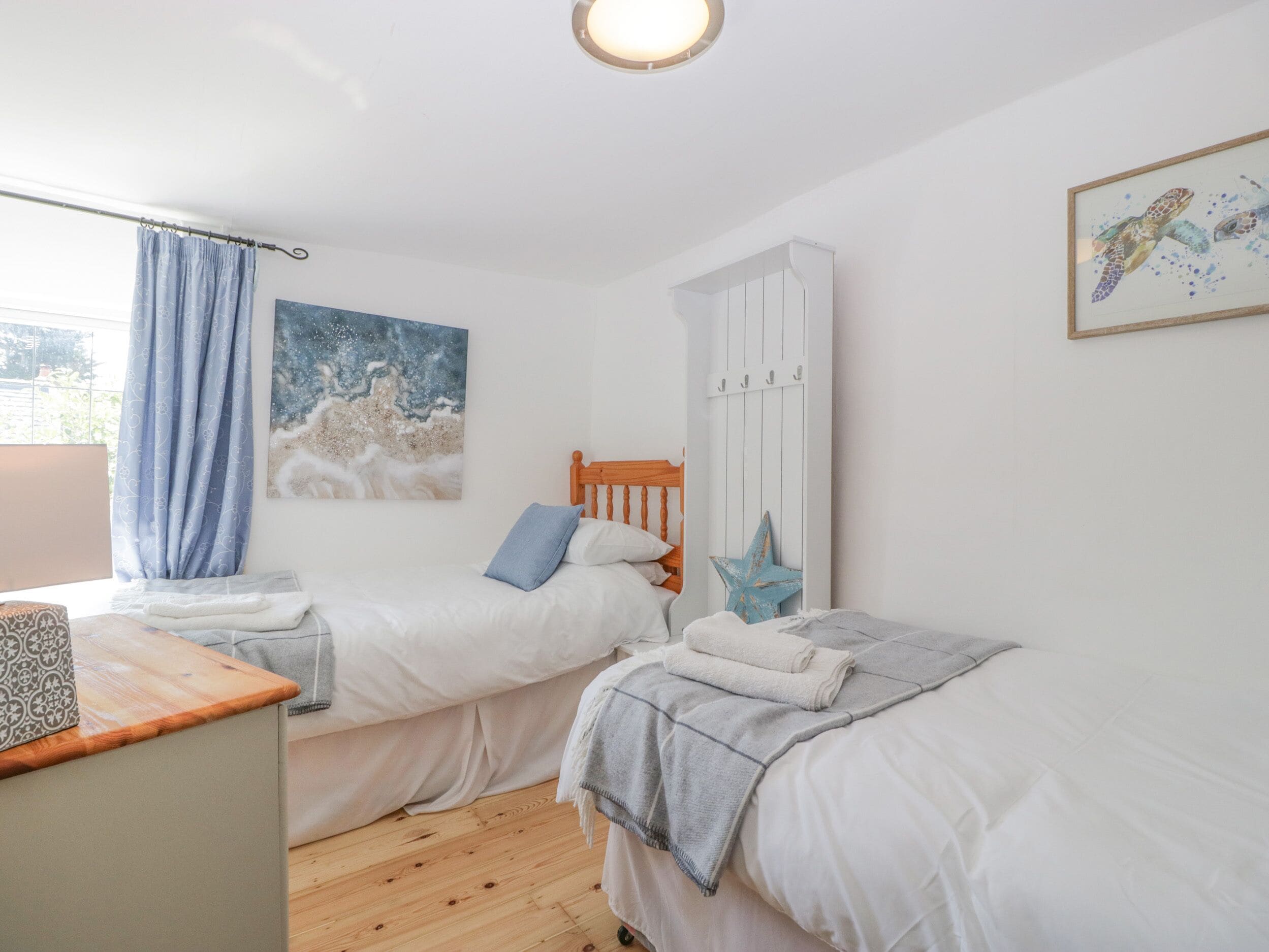 A bedroom with two single beds, a wooden wardrobe, a desk, and a window with curtains.