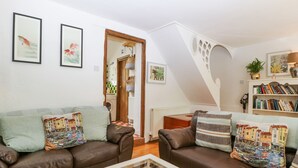 A cozy living room with two brown leather sofas, a glass coffee table, and a bookshelf filled with books. - Mackerel Cottage (Budleigh Salterton)