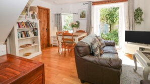 A cozy living room with a wooden dining table, a leather sofa, and a bookshelf. - Mackerel Cottage (Budleigh Salterton)