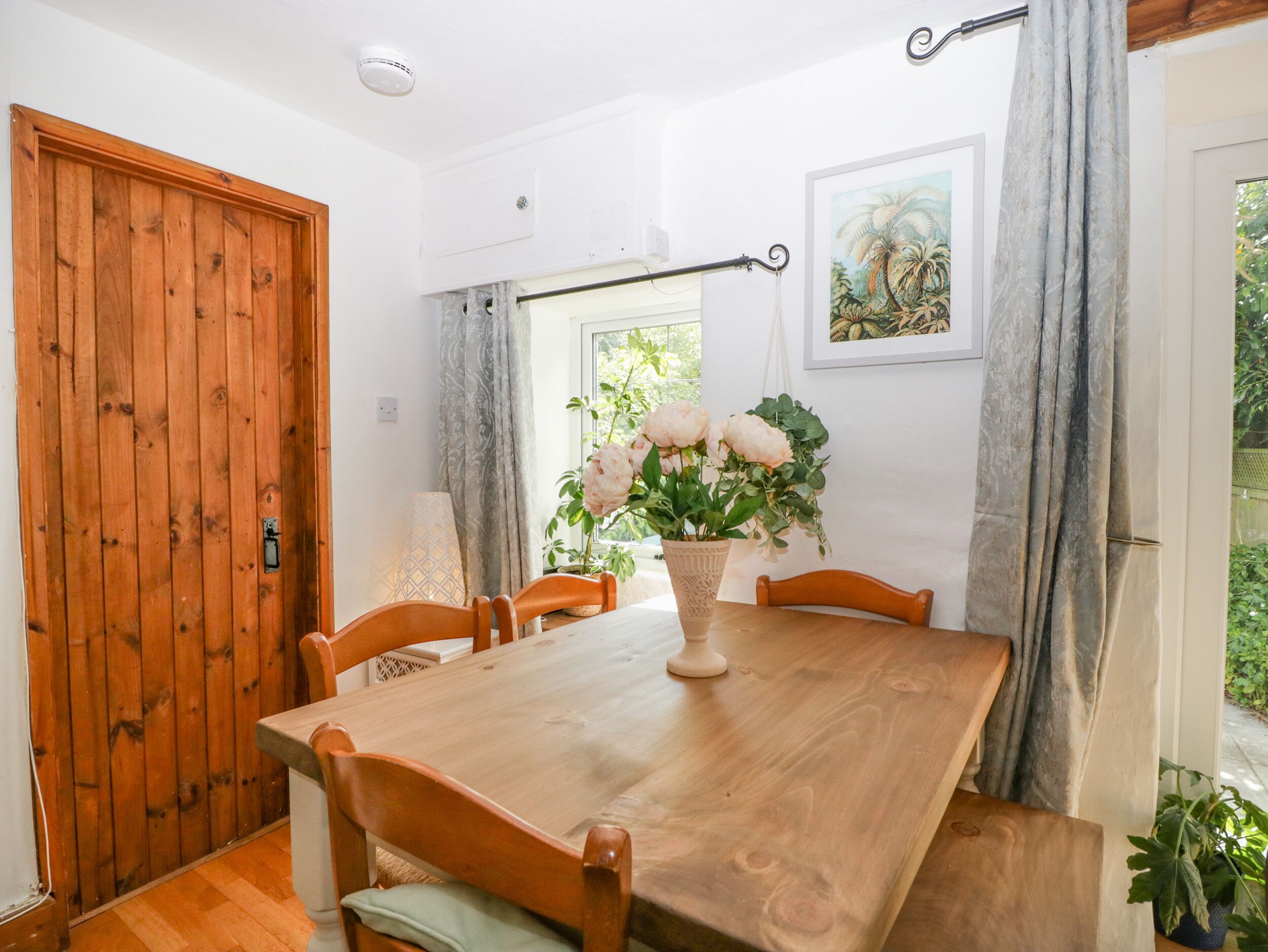 A dining area with a wooden table and chairs, a potted plant, and a window with curtains.