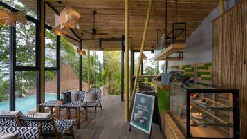 A modern interior with wooden flooring, patterned furniture, a glass display case, and large windows offering a view of greenery.