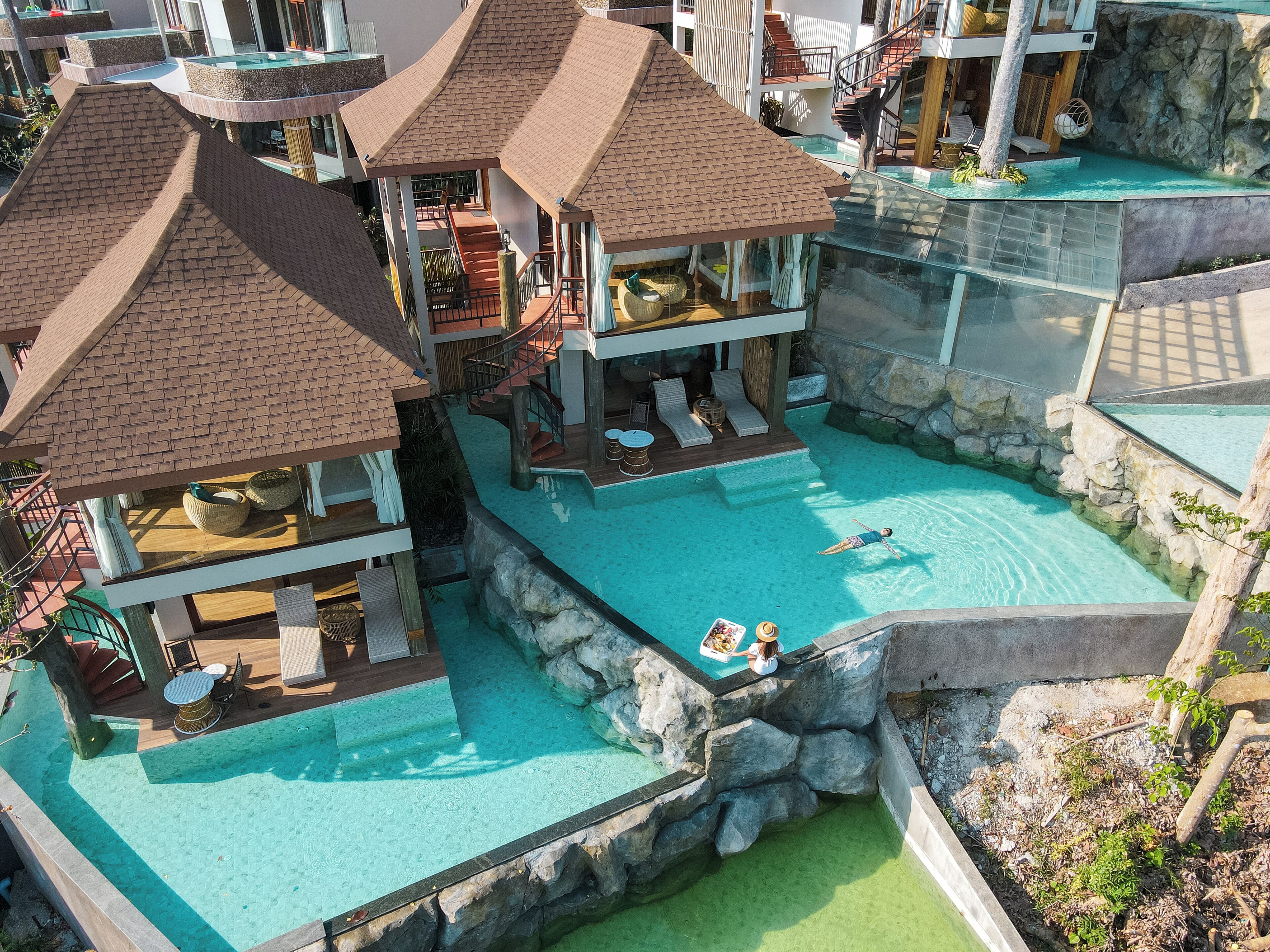 A resort with multiple swimming pools, lounge areas, and a central pool with a rocky edge.