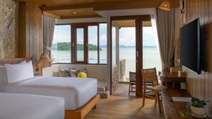 Une chambre avec un grand lit, un bureau et une télévision. La chambre offre une vue sur la mer et dispose d’un balcon avec une chaise.