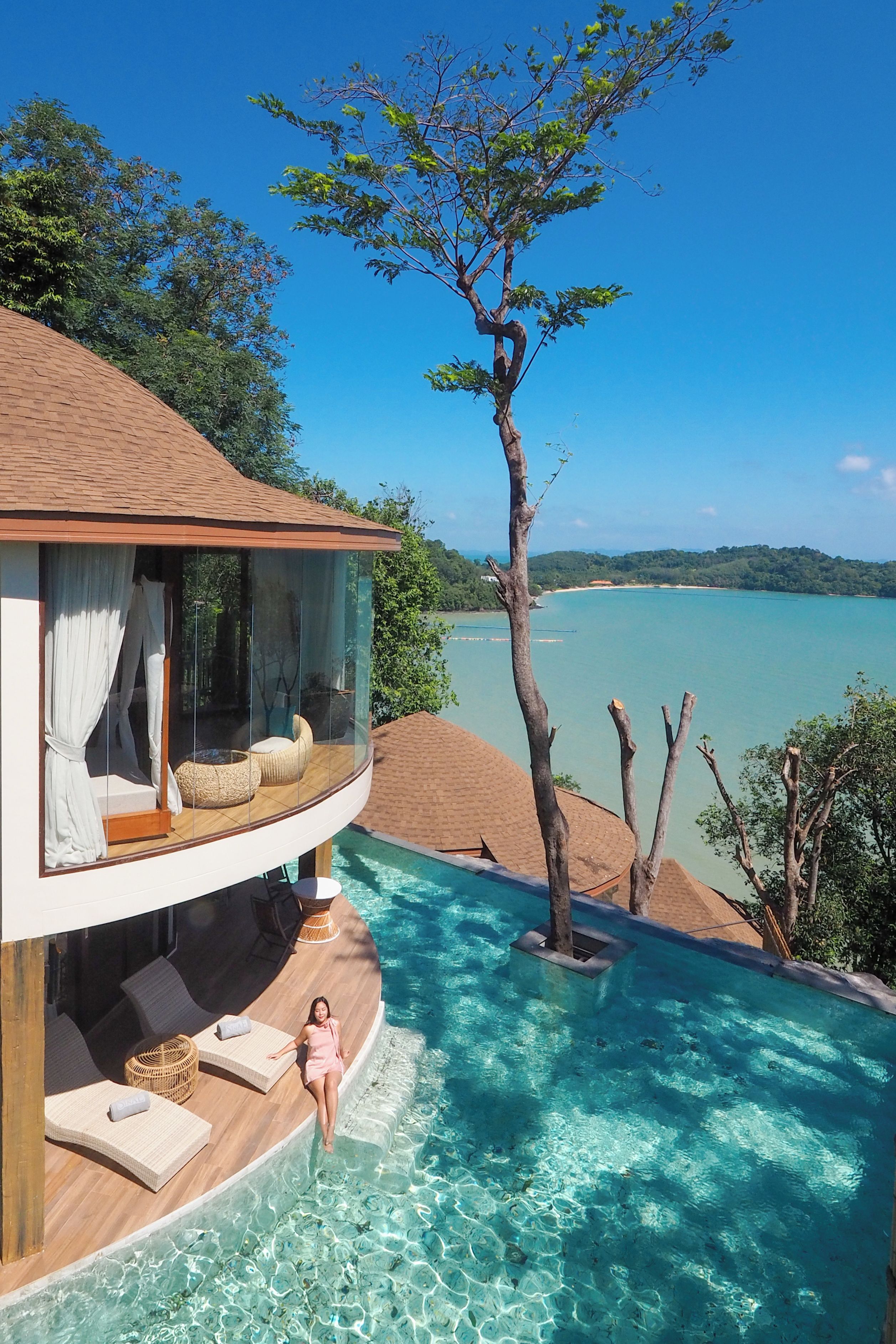 A modern villa with a glass infinity pool, a private balcony, and a view of the sea.