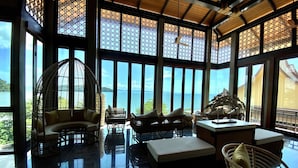 A spacious room with large windows offering a view of the sea, wicker furniture, and a ceiling fan. - SINAE Phuket Luxury Hotel (Ratsada)