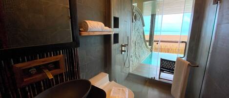Un bany modern amb un lavabo gran, vàter i plat de dutxa amb envidriera i vistes a la platja.