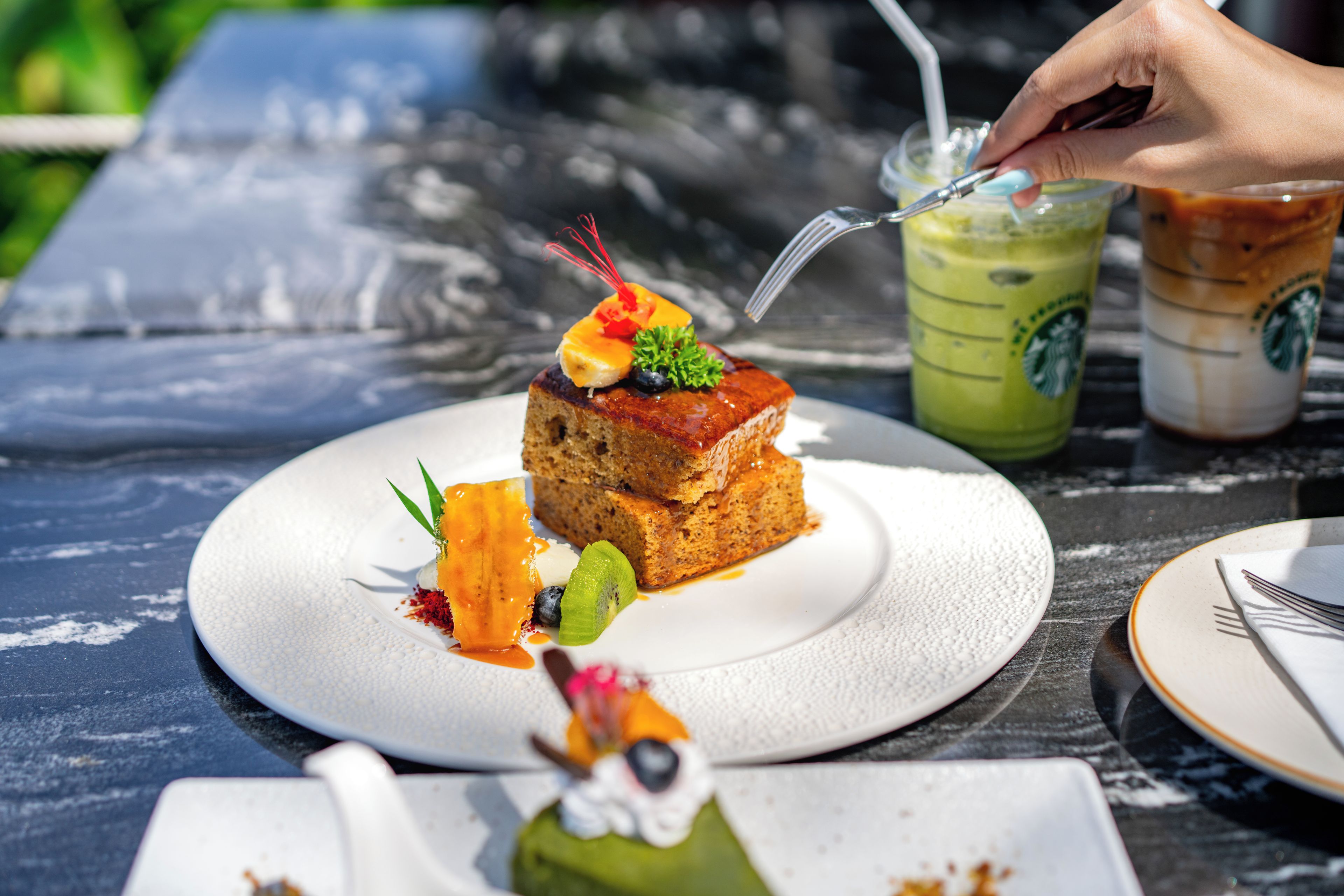 A dessert on a white plate with a fork and two Starbucks drinks on the table.