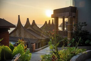 Un edificio tradicional con techos puntiagudos, estructura de bambú y vista al mar al atardecer.
