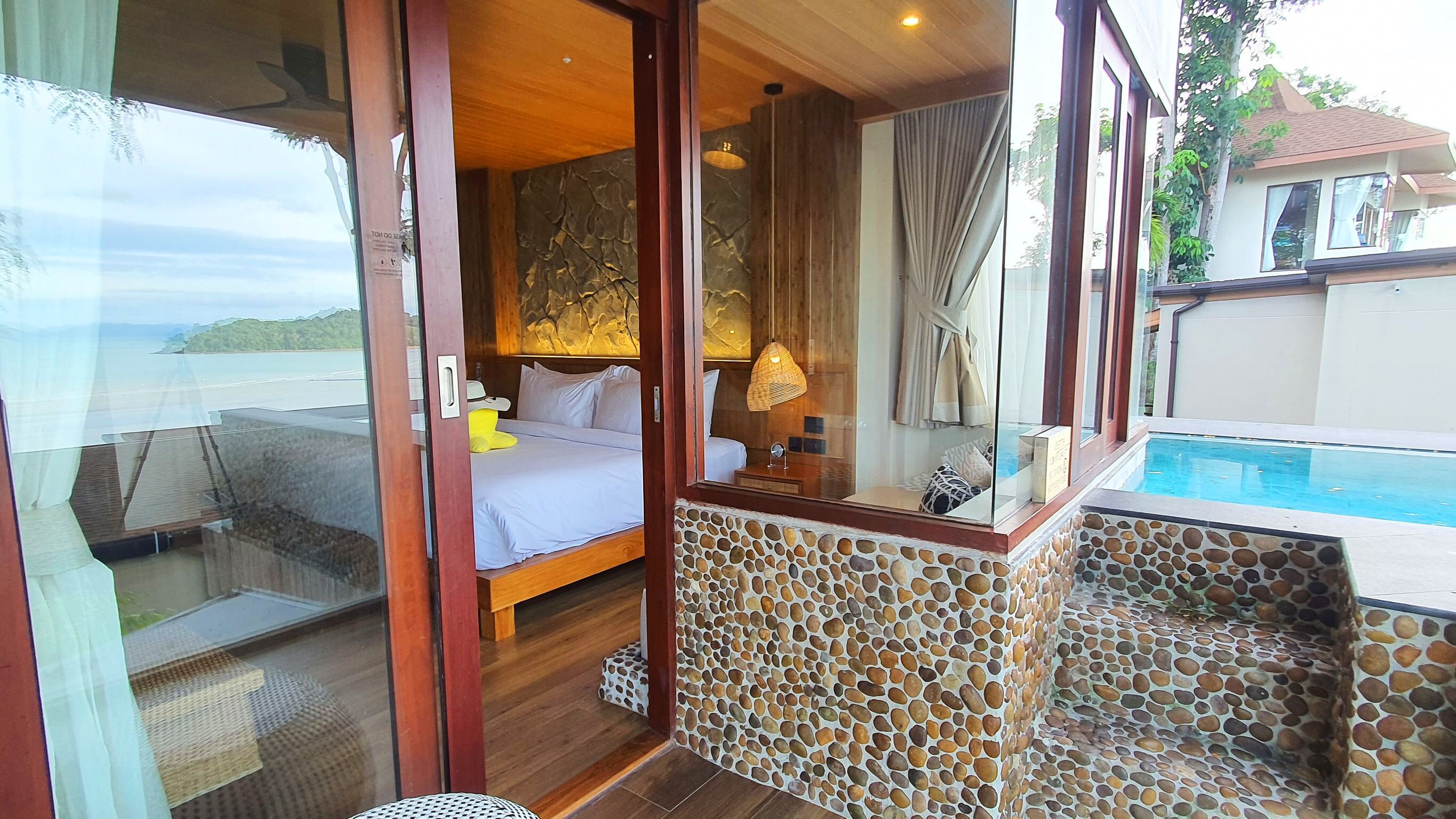 A bedroom with a large bed, a wooden ceiling, and a view of the sea.