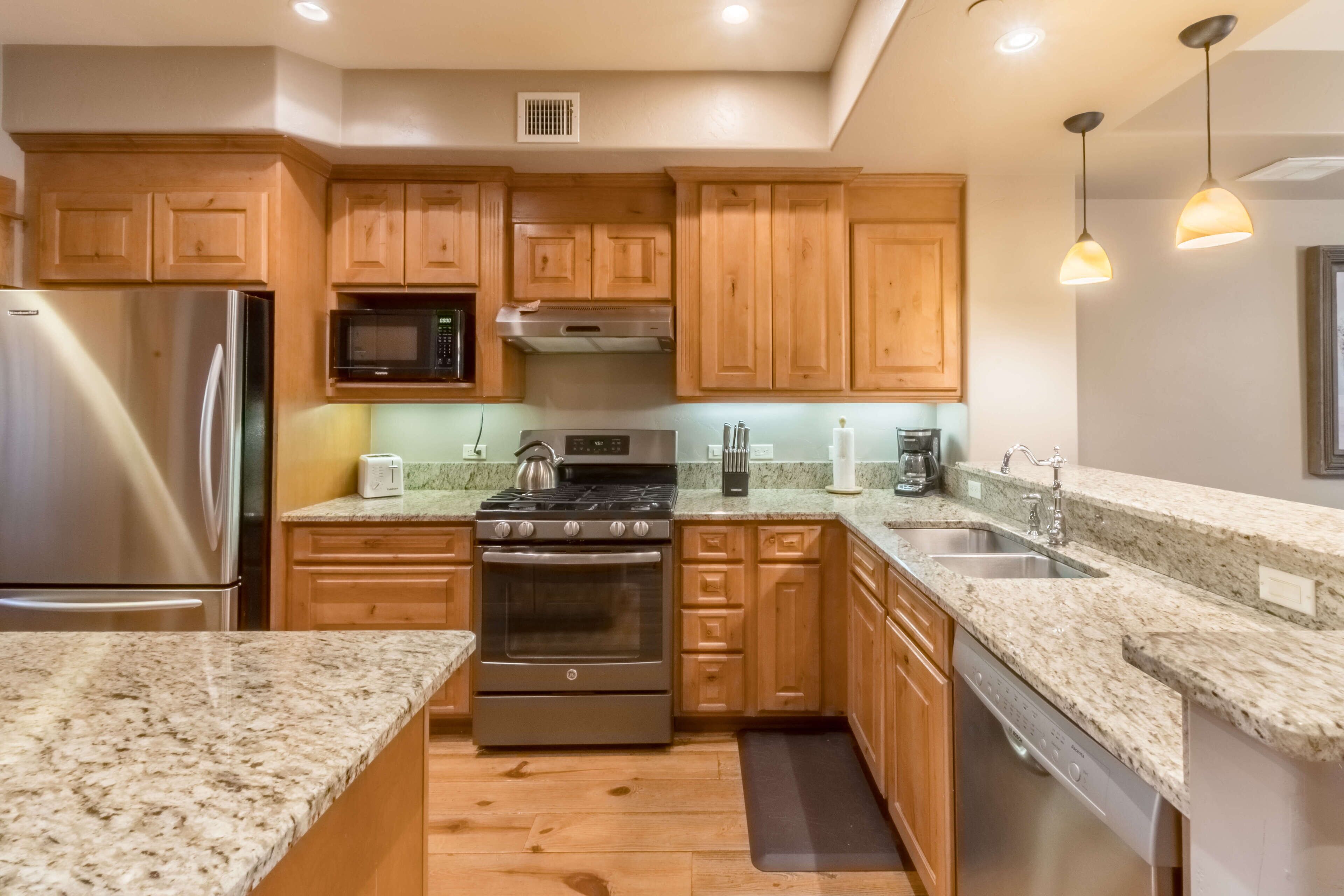 A modern kitchen with granite countertops, stainless steel appliances, wooden cabinets, and pendant lighting.
