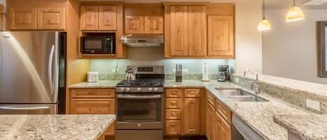 A modern kitchen with granite countertops, stainless steel appliances, wooden cabinets, and pendant lighting.