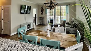 A spacious living room with a chandelier, a television, and a dining area with chairs and a table.