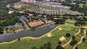 An aerial view of a residential area with a lake, golf course, and a large building with a red roof.