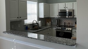 A kitchen with white cabinets, a granite countertop, a built-in oven, and a microwave.