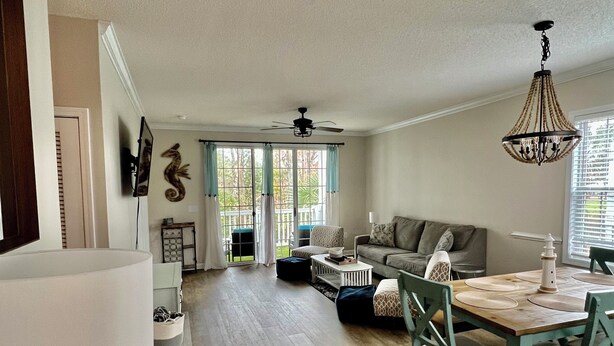 A spacious living area with a wooden floor, a dining table with chairs, a sofa, and a ceiling fan.