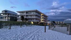 Een meerlaags hotel met balkons, een zandstrand op de voorgrond en een bewolkte lucht.