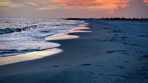 Een strand met golven, een zonsondergang en een verre kustlijn.