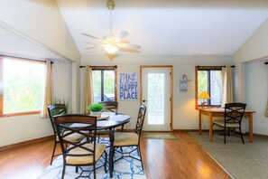 A dining area with a round table, four chairs, a ceiling fan, and a view of a lake through a window.