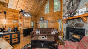 A cozy cabin interior with wooden walls, a stone fireplace, a leather sofa, and a coffee table.