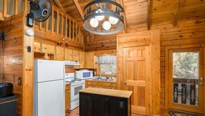A wooden cabin interior with a refrigerator, microwave, stove, and a small black cabinet.