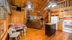 A wooden cabin interior with a dining table, sofa, kitchen area, and a staircase.