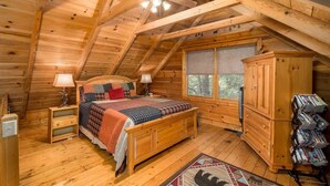 A wooden cabin bedroom with a bed, nightstands, a dresser, and a window.