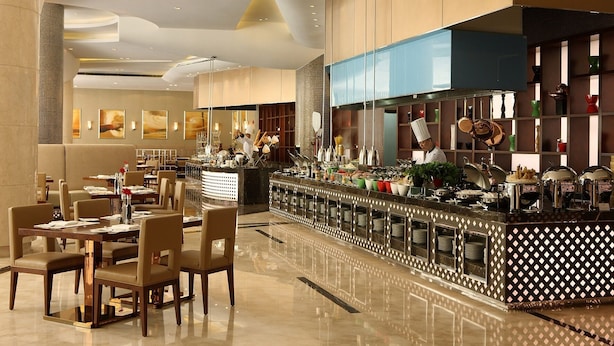 A modern hotel restaurant with a long counter, multiple dining tables, and a kitchen area visible. - Tianjin Crown International Apartments (Tianjin)