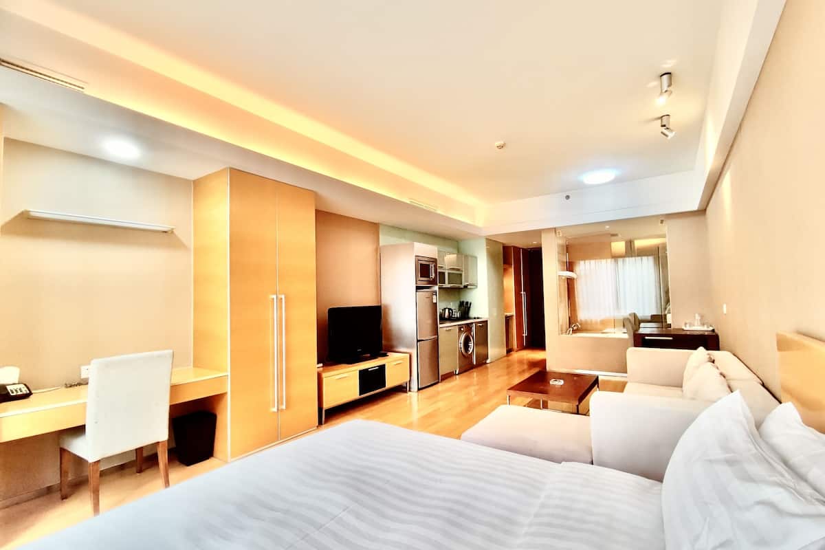 Une chambre d’hôtel moderne équipée d’un grand lit, d’un bureau, d’une télévision, d’une kitchenette et d’une salle de bain.