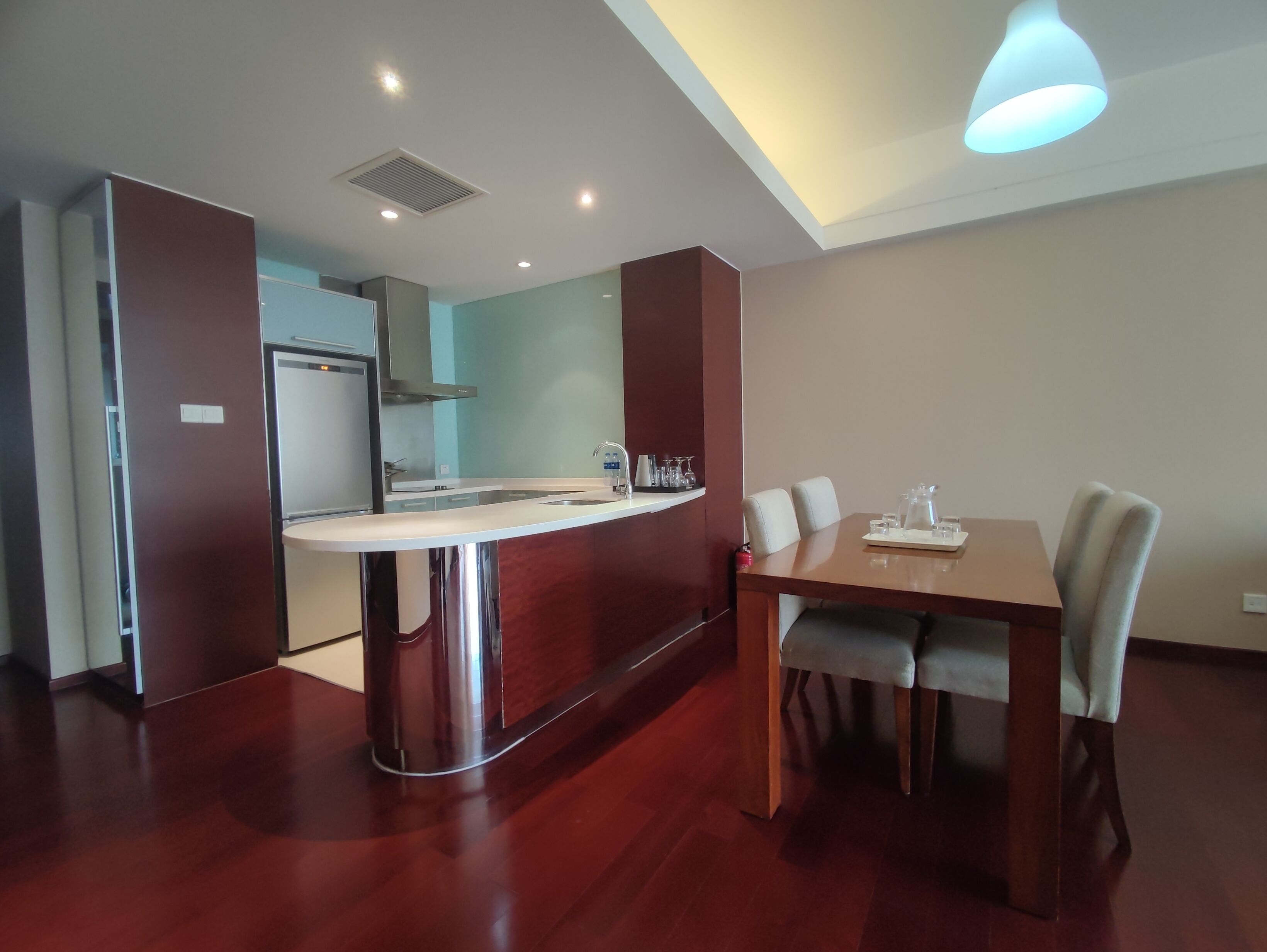 A modern kitchen with a central island, a dining area with a wooden table and chairs, and a ceiling with recessed lighting.