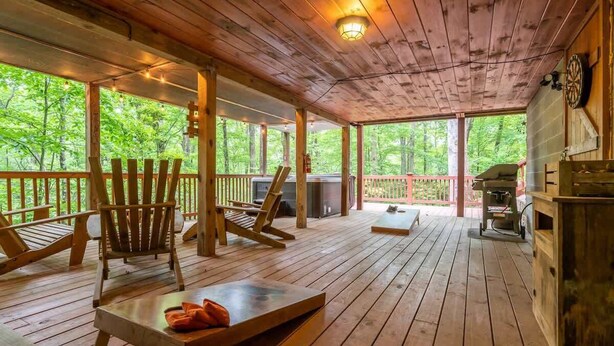Una terraza de madera con mobiliario exterior, una parrilla y vistas al bosque.