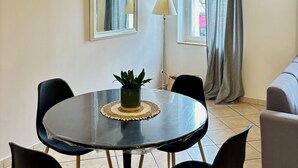 Un comedor con una mesa redonda, cuatro sillas, una planta en maceta, dos lámparas de pared y un ventanal con cortinas grises.