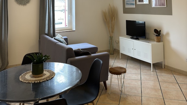 Una sala de estar moderna con comedor, sofá gris, televisor de pantalla plana y arte decorativo en la pared.