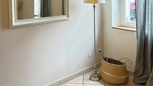 Una habitación con un espejo grande, una lámpara de pie, una ventana con cortinas y una cesta tejida en el suelo.