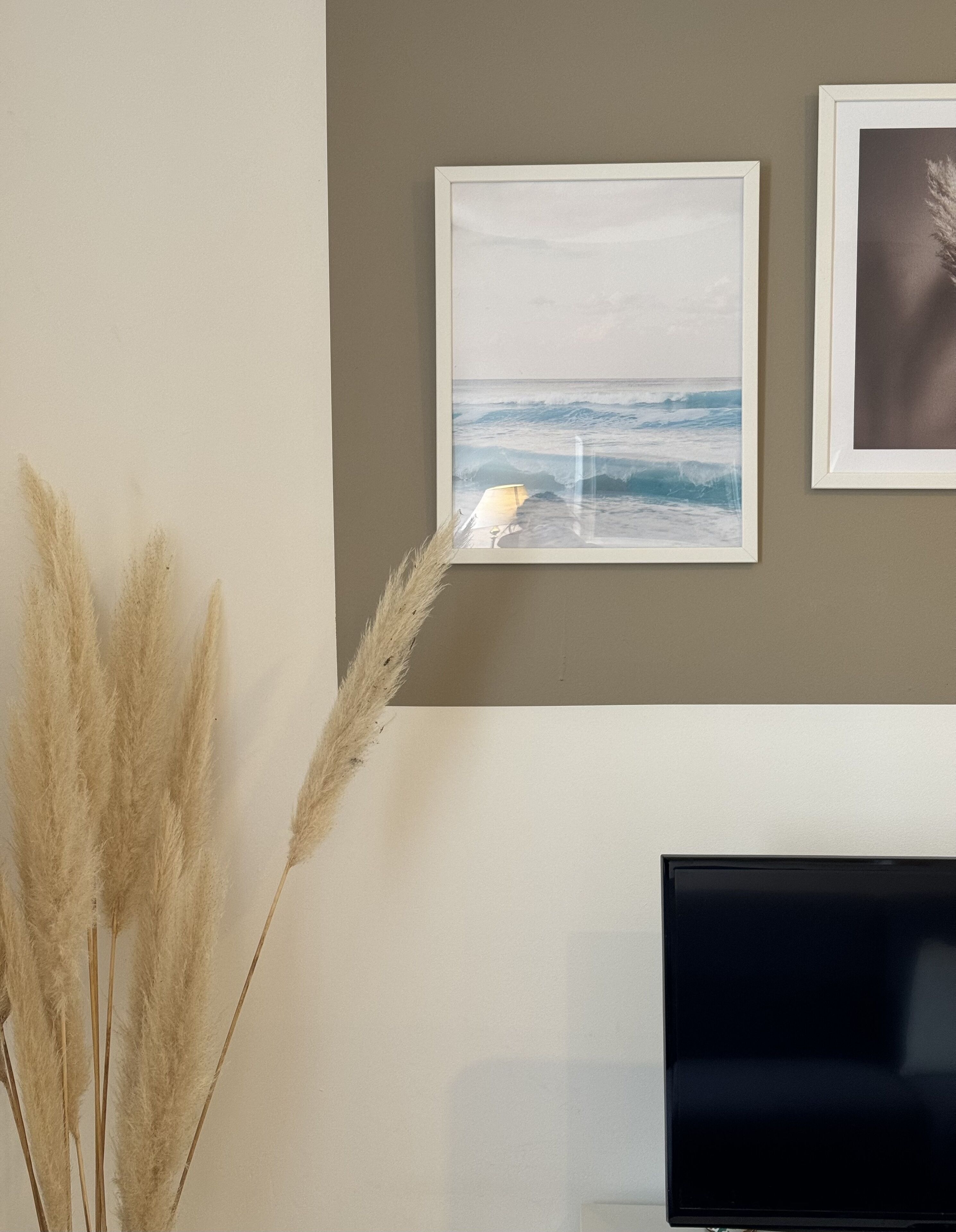 A wall with two framed pictures, one depicting a beach scene and the other a portrait.