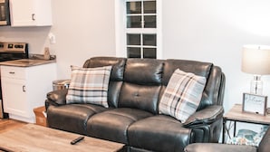 A living room with a leather sofa, wooden coffee table, and a kitchen area in the background. - Private - Secluded Cabin, close to Windrock (Oliver Springs)