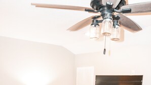 A living room with a wooden floor, a leather sofa, a coffee table, a TV stand with a flat-screen TV, a ceiling fan with three lights, and a checkered wall decoration. - Private - Secluded Cabin, close to Windrock (Oliver Springs)