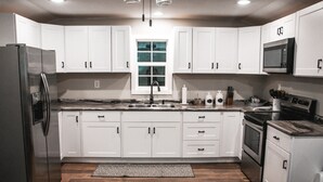 A modern kitchen with white cabinets, stainless steel appliances, and a central window. - Private - Secluded Cabin, close to Windrock (Oliver Springs)