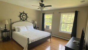 A bedroom with a bed, a ceiling fan, a ship's wheel decoration, two windows, and a dresser. - Bar Harbor Serenity close to Hadley Point Beach (Bar Harbor)