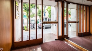 Een hotelingang met een glazen deur, een rode loper en zicht op geparkeerde auto's en gebouwen.