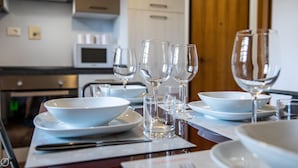 Eettafel gedekt met witte borden, kommen en wijnglazen, met een magnetron en kastjes op de achtergrond.