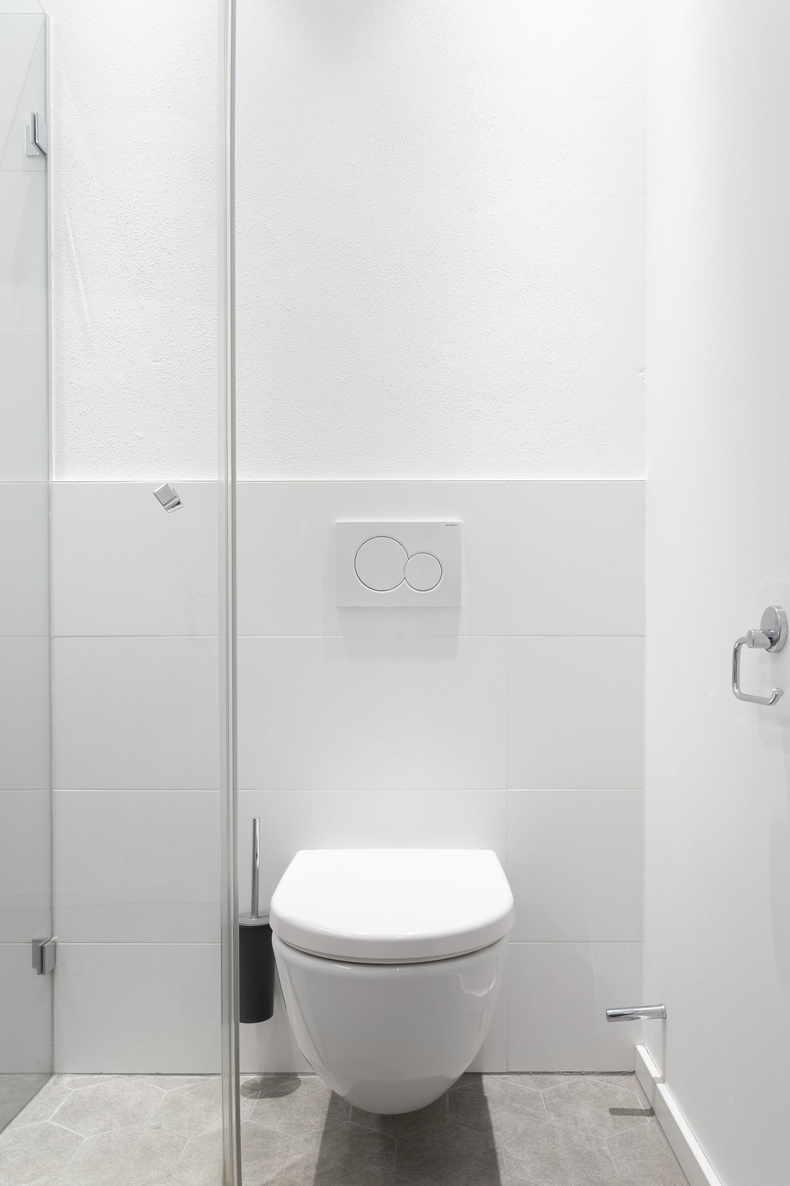 A modern bathroom with a toilet, a hand dryer, and a wall-mounted flush button.