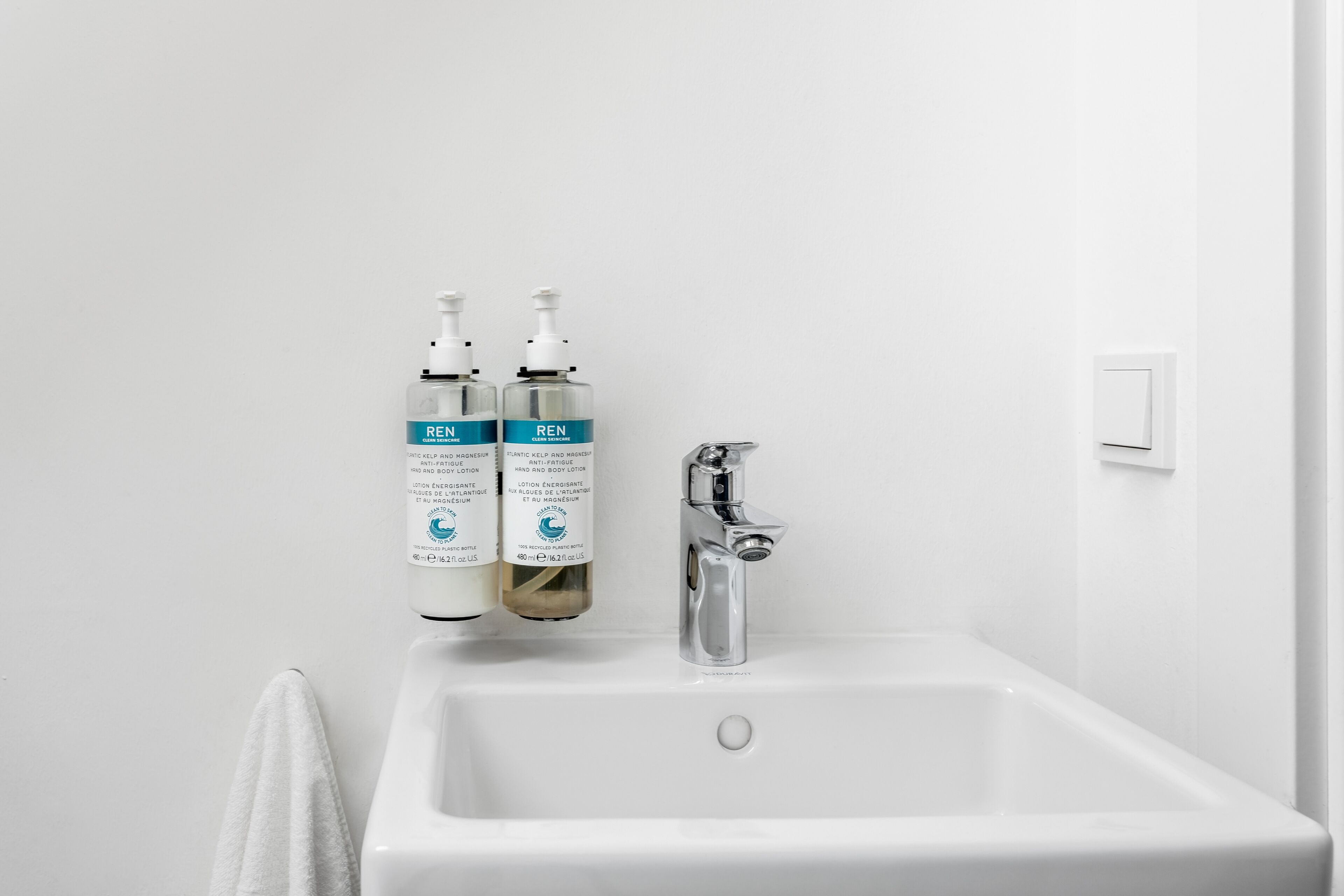 A bathroom with a white sink, two bottles of REN body lotion, and a silver faucet.