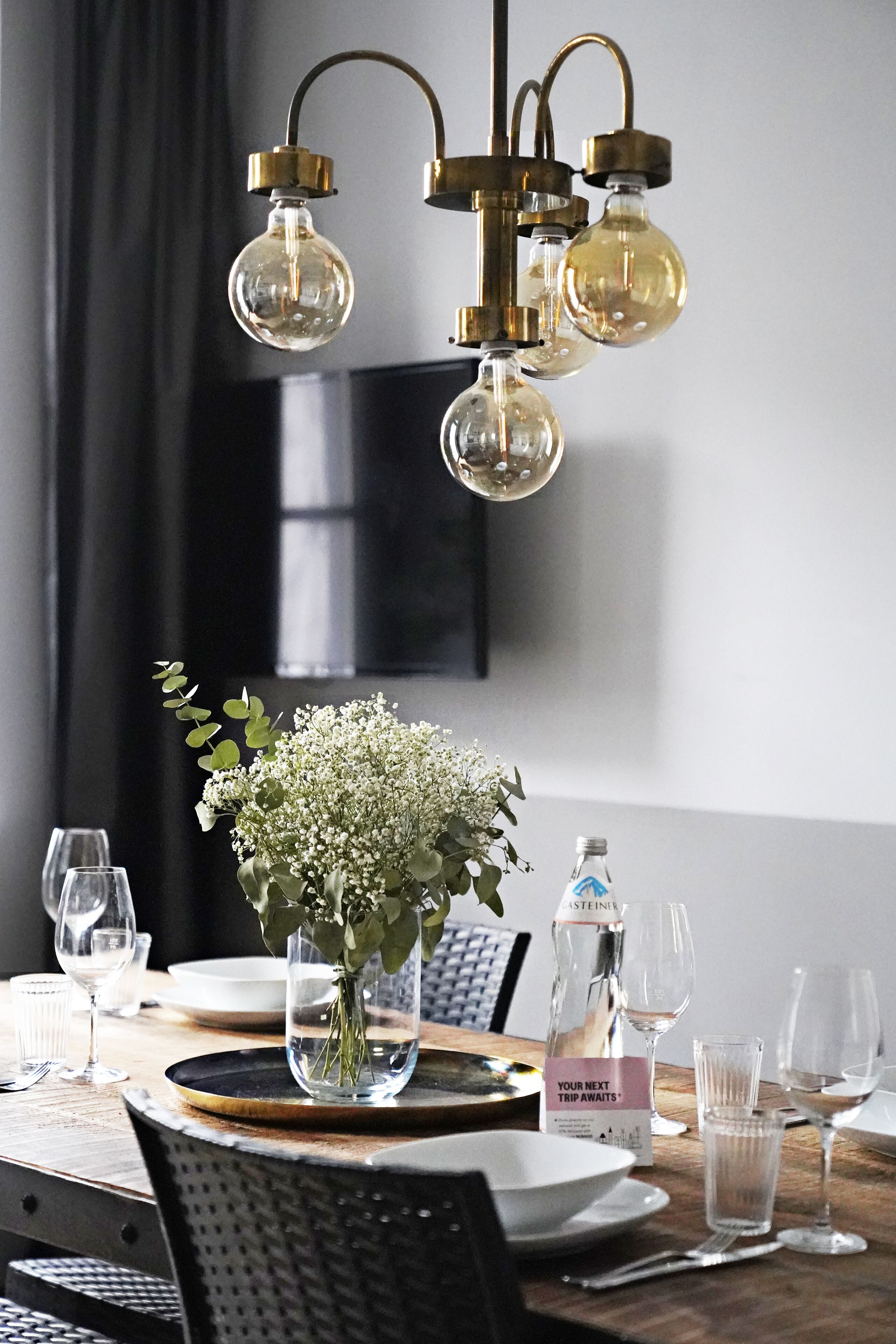 Una mesa de comedor dispuesta con platos, vasos y un florero con flores.