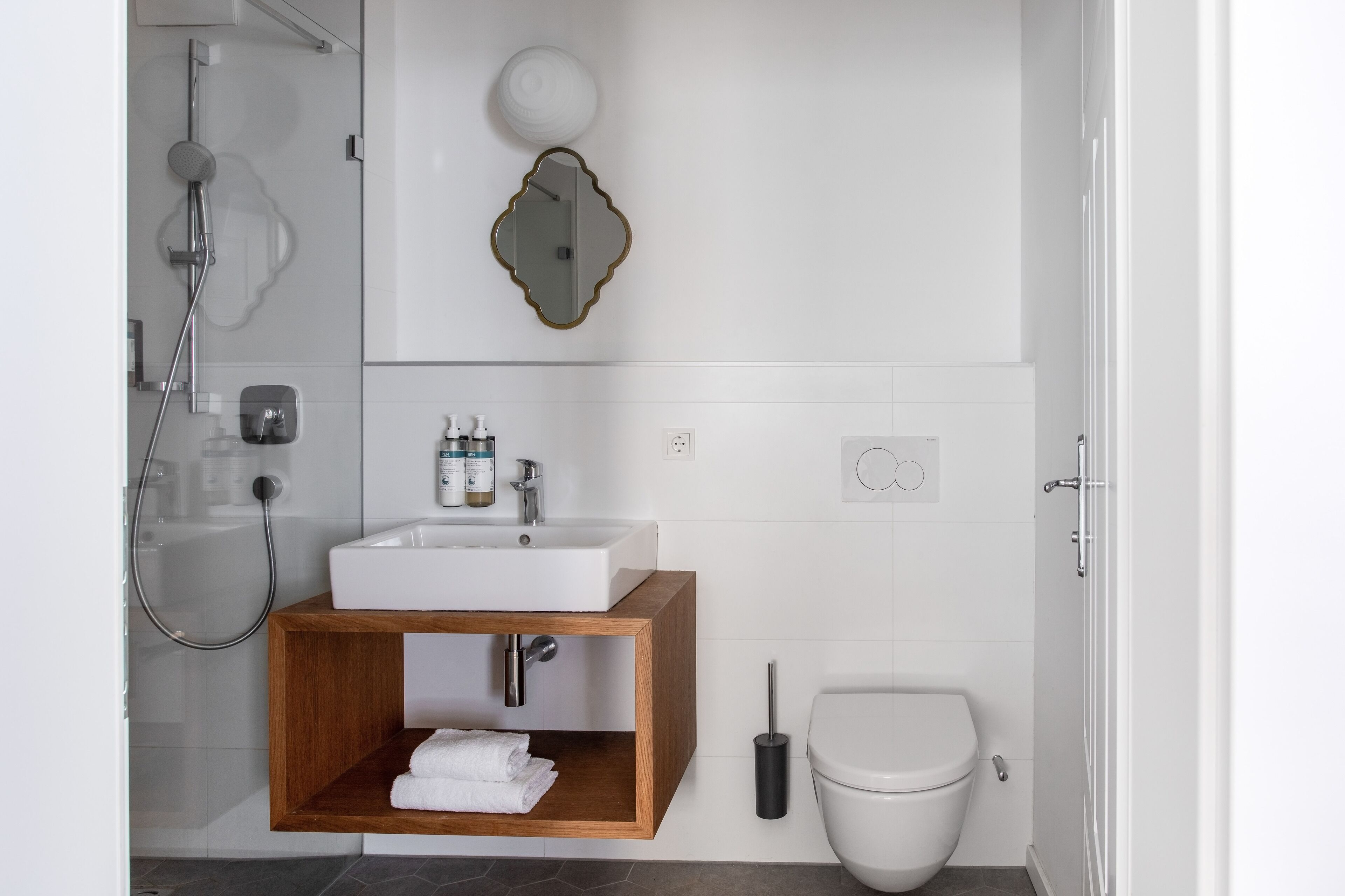 Un baño moderno con lavamanos blanco, tocador de madera y un inodoro.
