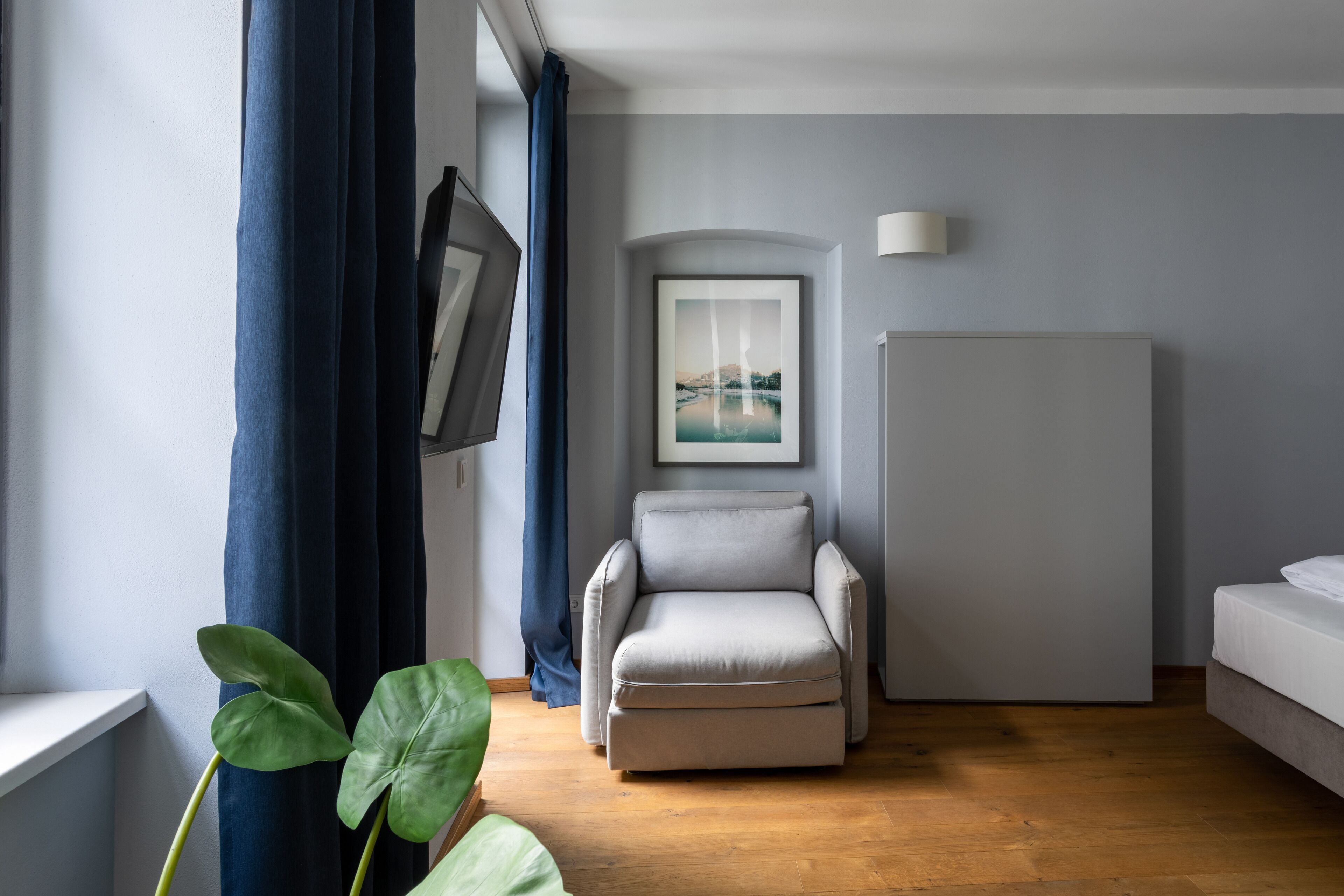 A modern room with a grey armchair, a white sofa, a framed picture on the wall, and a large plant.