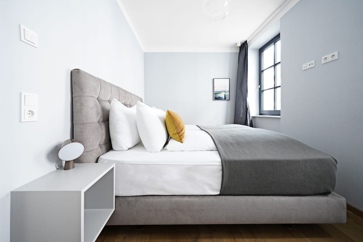 A modern bedroom with a bed, bedside table, and a window.