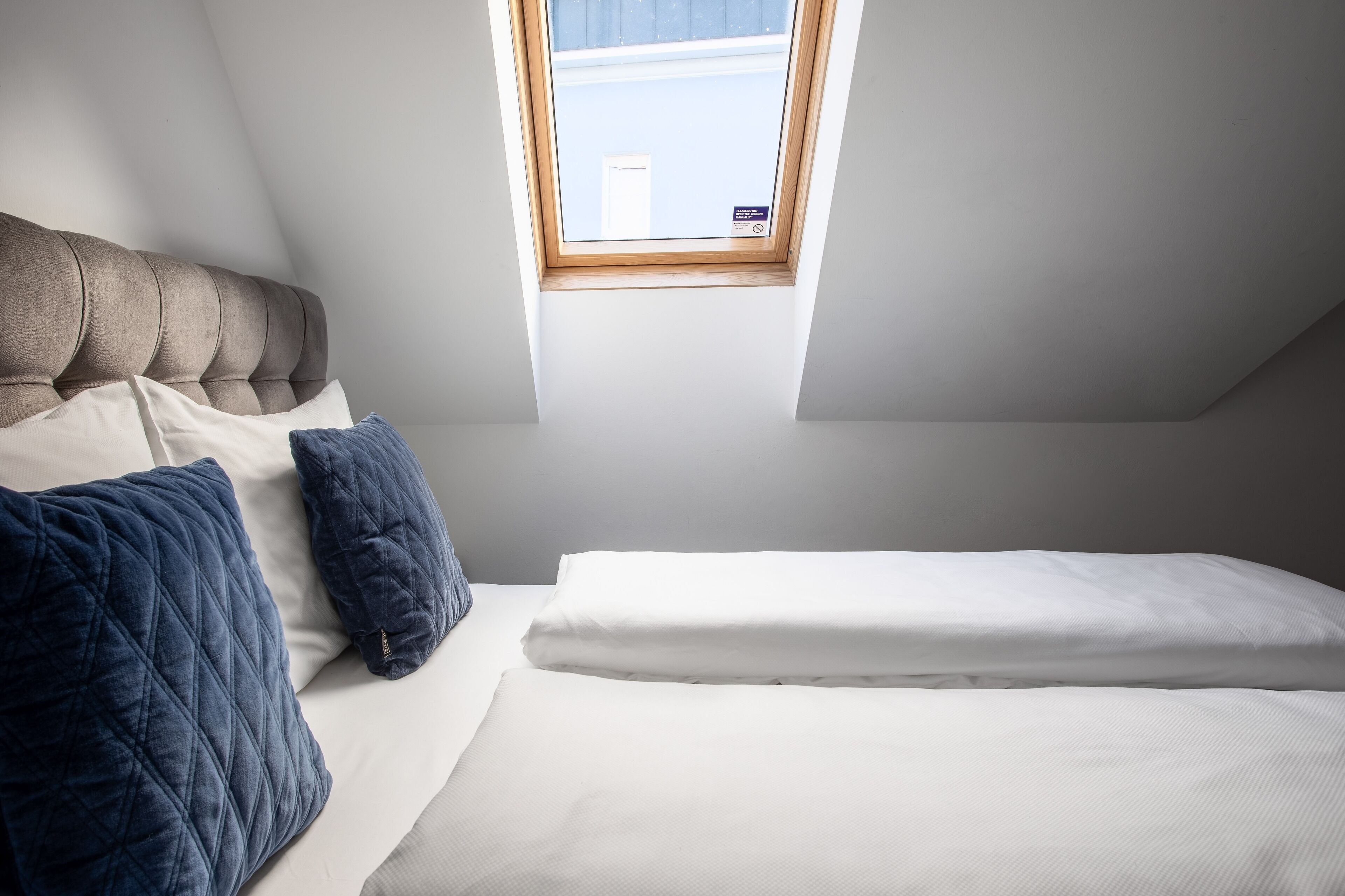 A bedroom with a sloped ceiling, a window, and a bed with pillows.